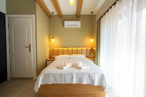 A hotel room with a bed, bedside lamps, an air conditioner, a door, and a window with curtains. - Derya Guest House (Ayvalık)