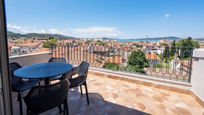 Un balcon avec une table et des chaises, d’où l’on peut admirer la vue sur une ville avec ses bâtiments et une montagne lointaine.