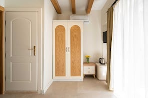 A room with a white door, a wardrobe with wooden doors, a small table with a vase of flowers, a kettle, and an air conditioning unit. - Derya Guest House (Ayvalık)