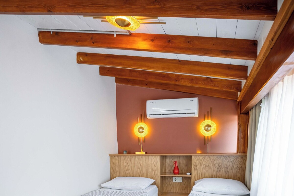 Un dormitorio con dos camas individuales, vigas de madera en el techo, un equipo de aire acondicionado y una mesita de noche con lámpara.