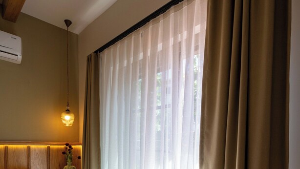 Une chambre d’hôtel avec un lit, une table de chevet avec une lampe et des rideaux légers.