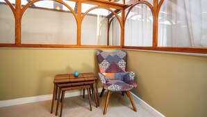 Une pièce avec un plafond en bois, une fenêtre avec des rideaux, une chaise à motifs et une petite table en bois sur laquelle est posé un vase.