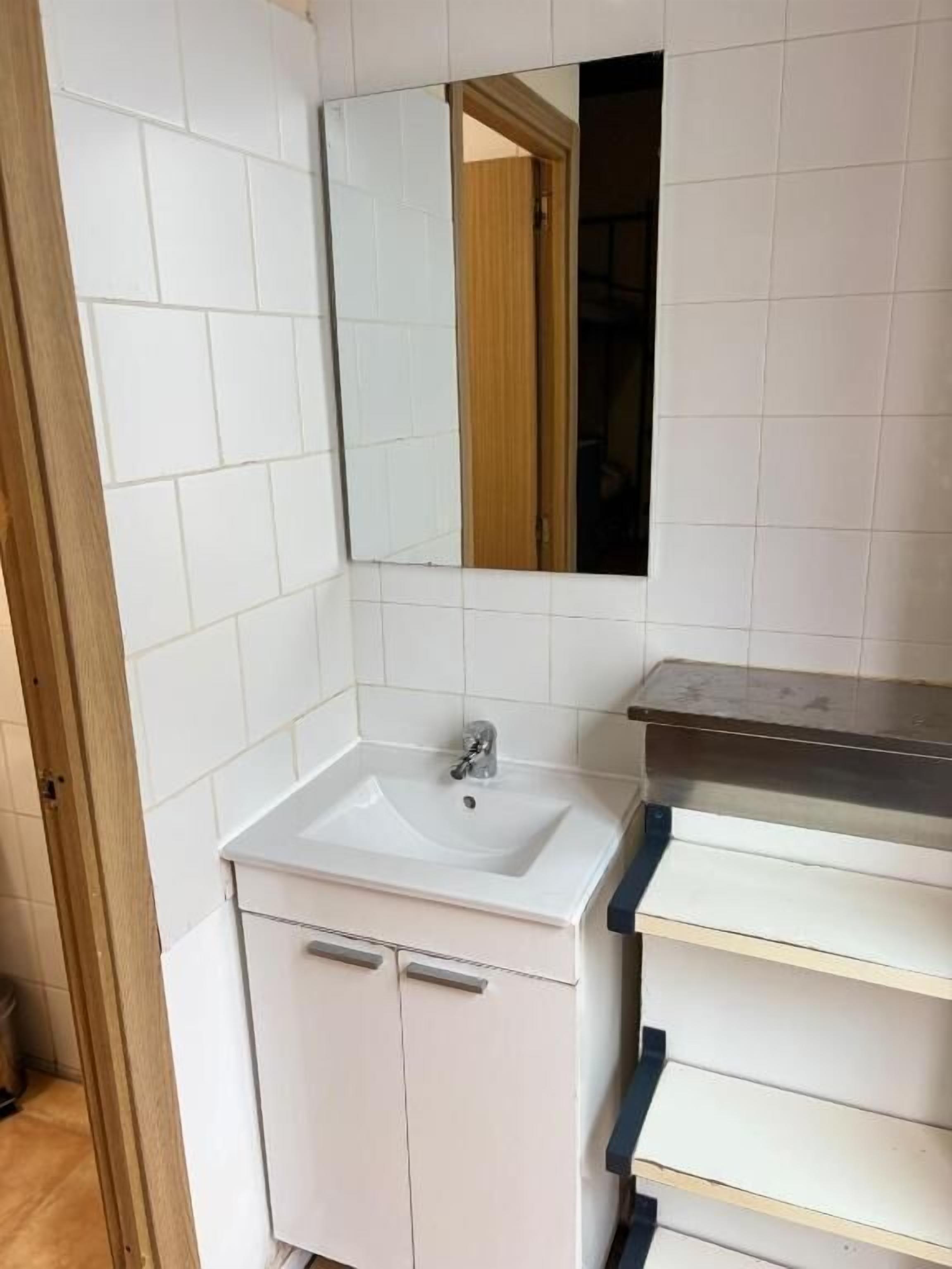 A bathroom with white tiles, a sink, a mirror, and a wooden door.