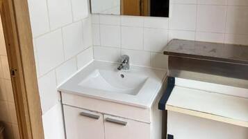 A bathroom with white tiles, a sink, a mirror, and a wooden door.
