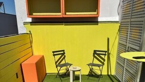 Un petit espace extérieur aménagé avec du gazon synthétique, deux chaises, une table et un meuble de rangement.