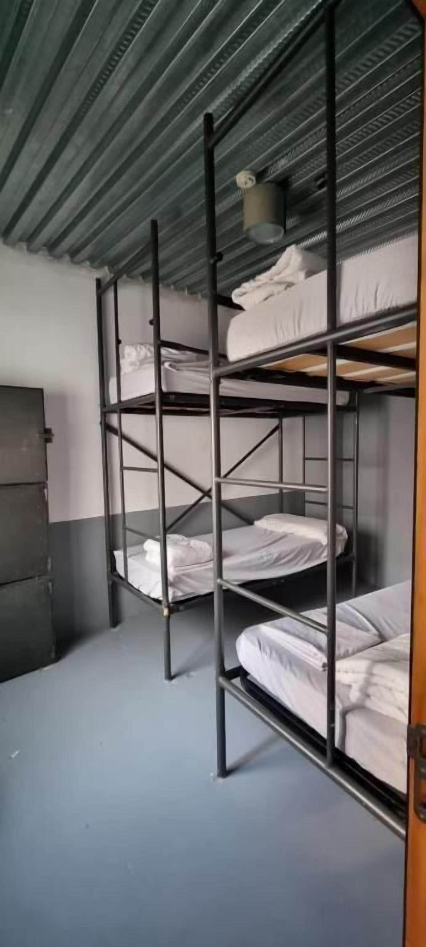 Camas literas en una habitación con techo de metal y una puerta a la izquierda.