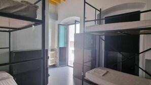 Une chambre de dortoir avec des lits superposés, une porte donnant sur un balcon et une fenêtre.