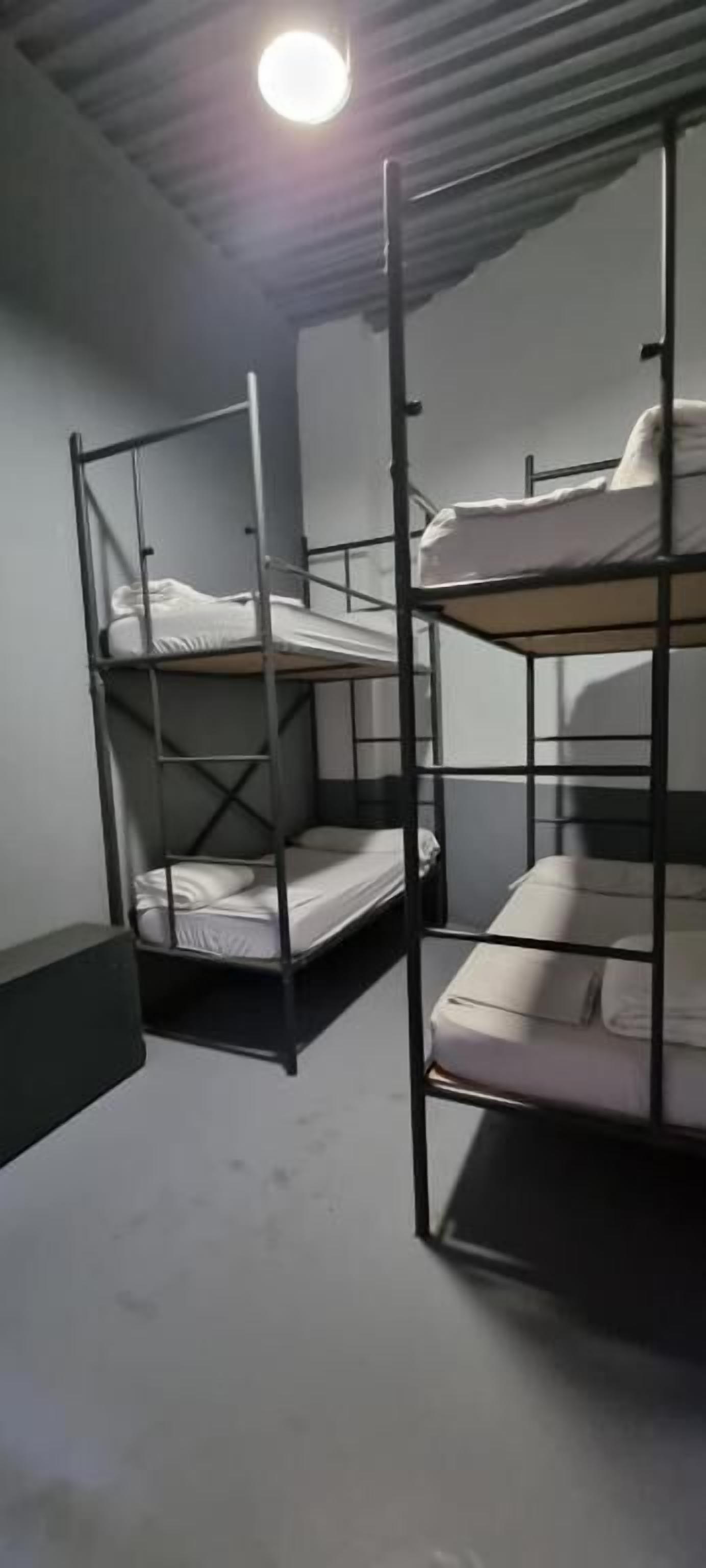 Llits superposats en una habitació amb sostre inclinat i una làmpada.