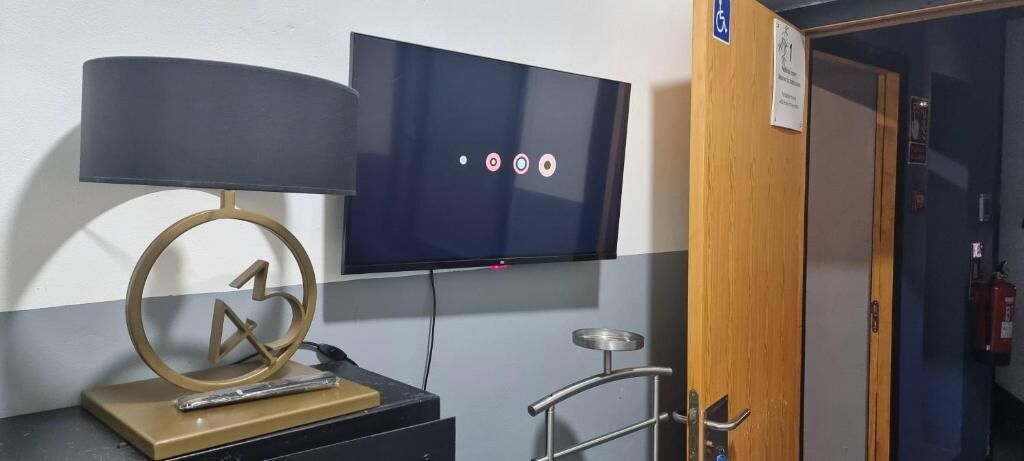 Une pièce avec un téléviseur fixé au mur, un bureau avec une lampe et une porte sur laquelle est accroché un extincteur.