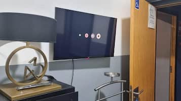 Una habitación con televisión en la pared, un escritorio con lámpara y una puerta con extintor.