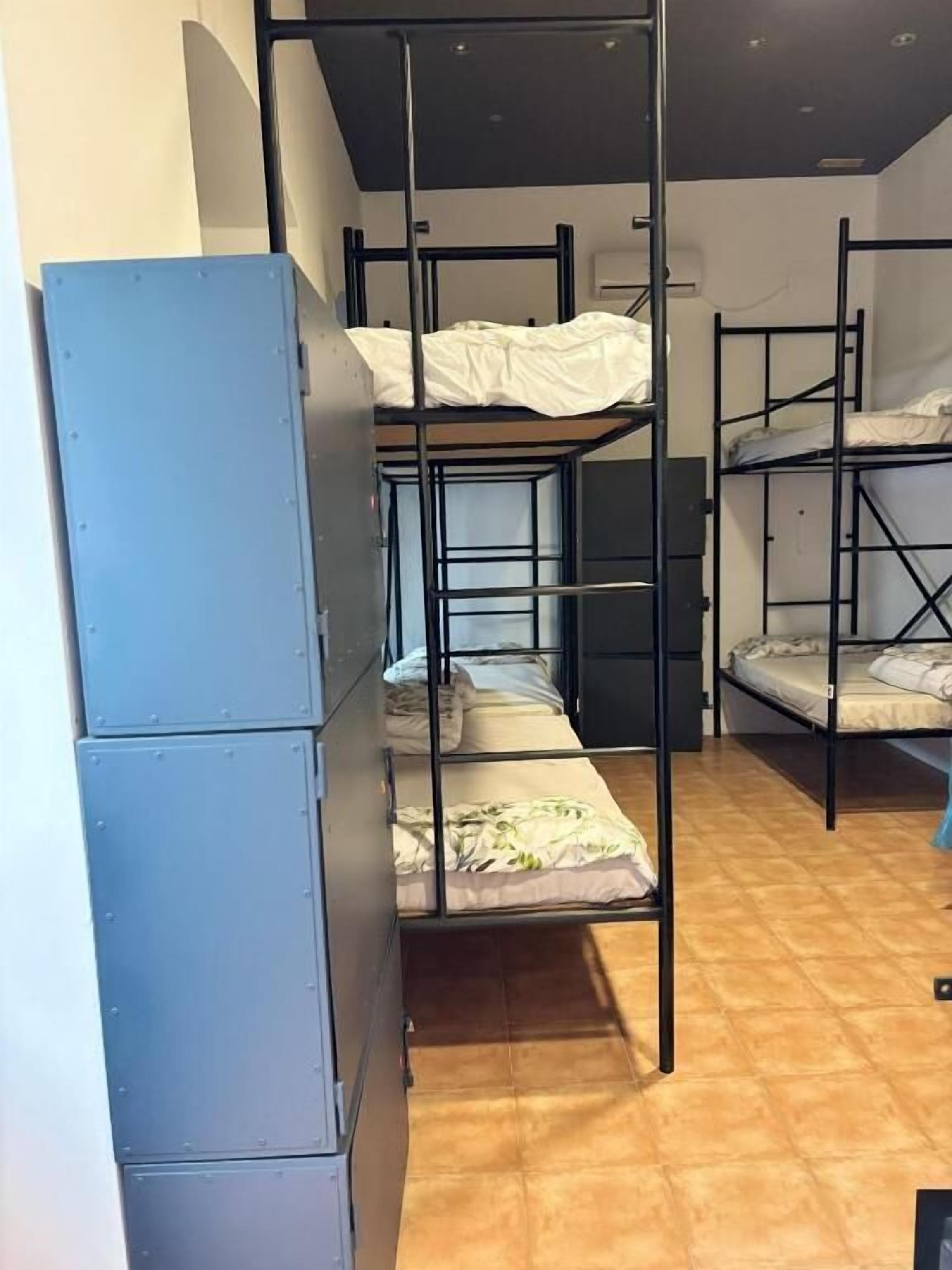 A dormitory room with bunk beds, a wardrobe, and a tiled floor.