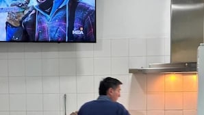Une cuisine où une personne est en train de cuisiner, un téléviseur fixé au mur et une bouteille de bière posée sur le comptoir.