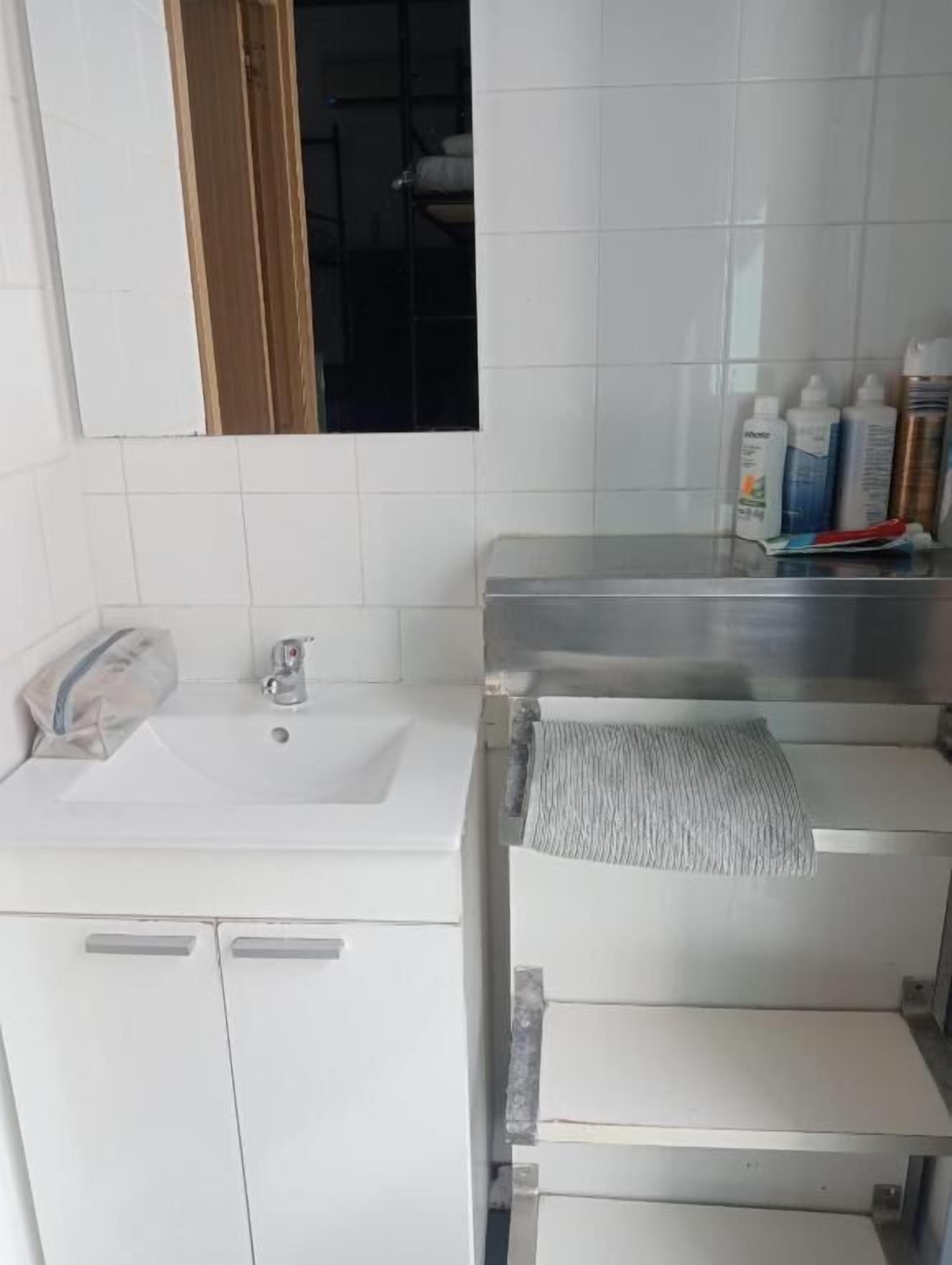 Un baño con lavamanos blanco, un espejo y una repisa con artículos de aseo.