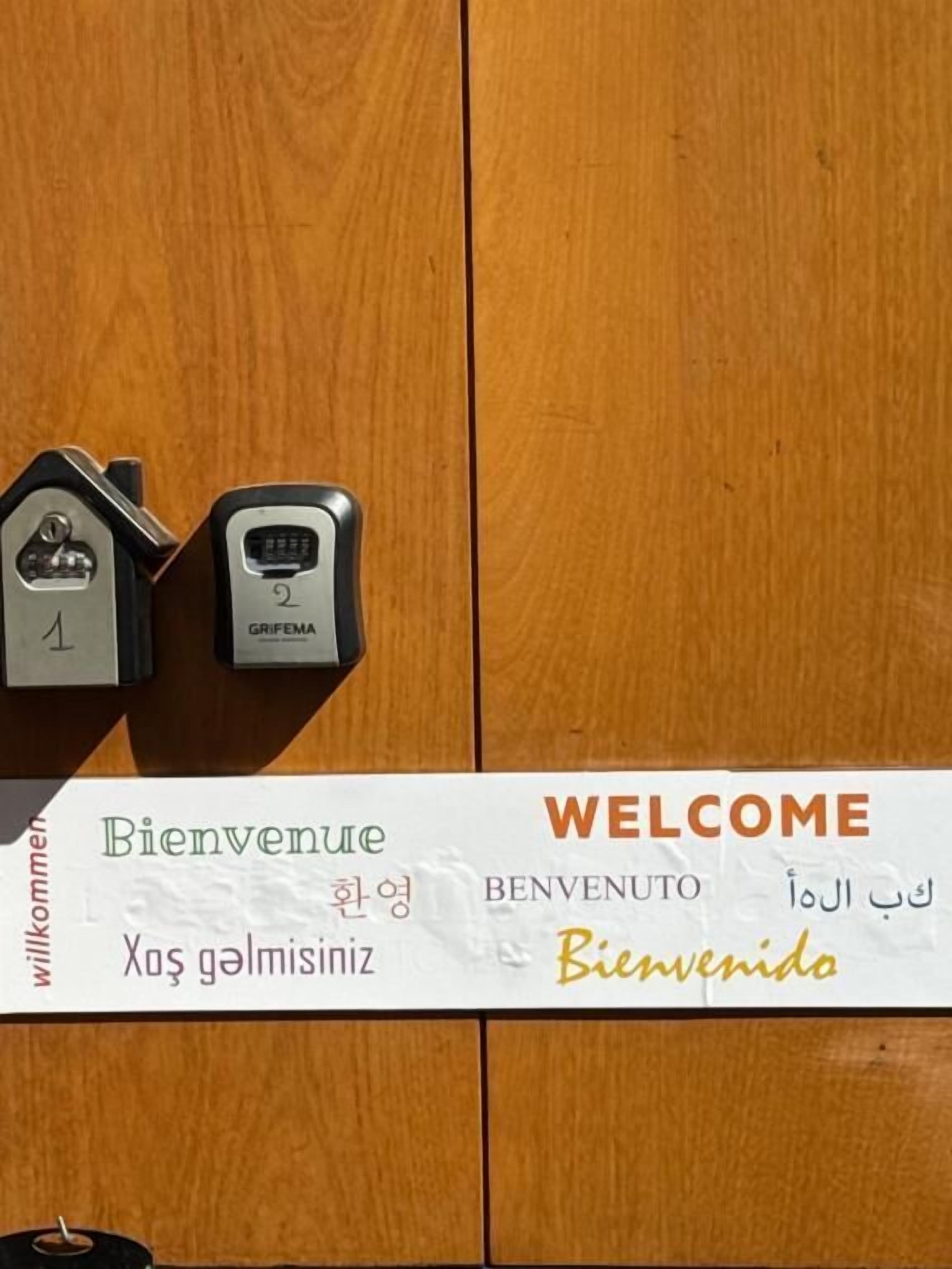 A welcome sign with multilingual greetings and two house-shaped key holders labeled '1' and '2'.
