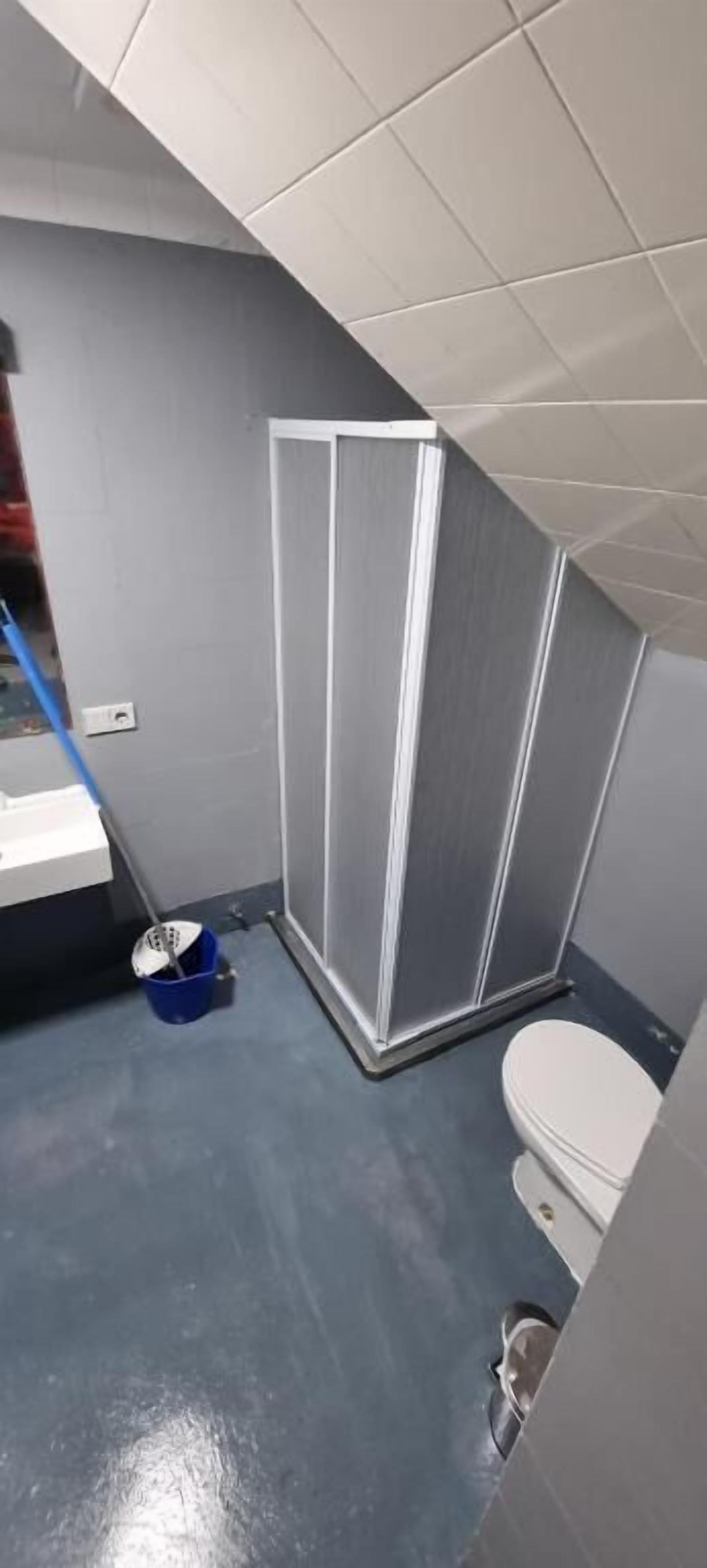 A bathroom with a shower, toilet, and a mop leaning against the wall.
