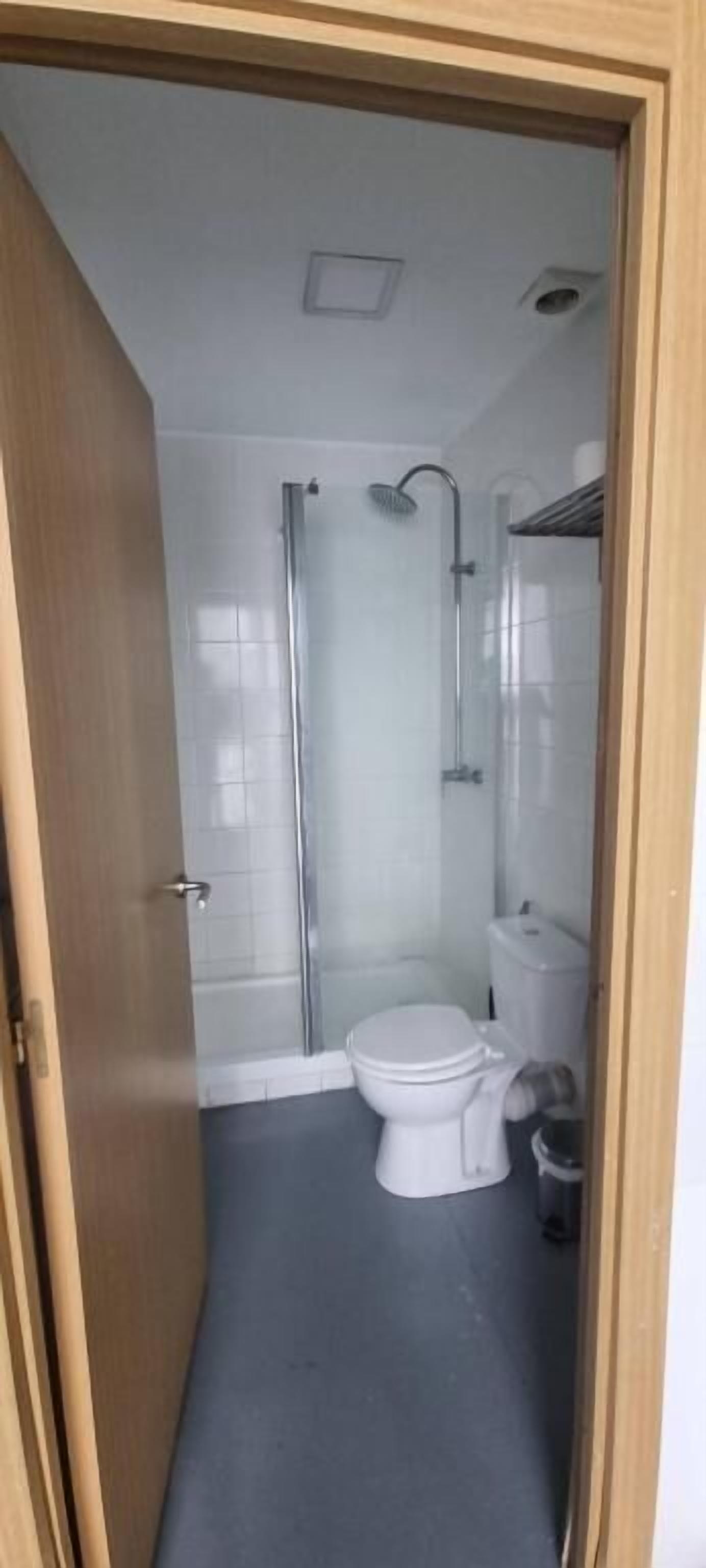 A compact bathroom with a shower, toilet, and a small trash bin.