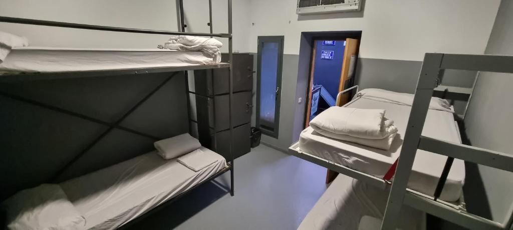 A dormitory room with bunk beds, a small window, and a door.