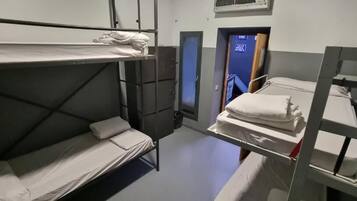 A dormitory room with bunk beds, a small window, and a door.