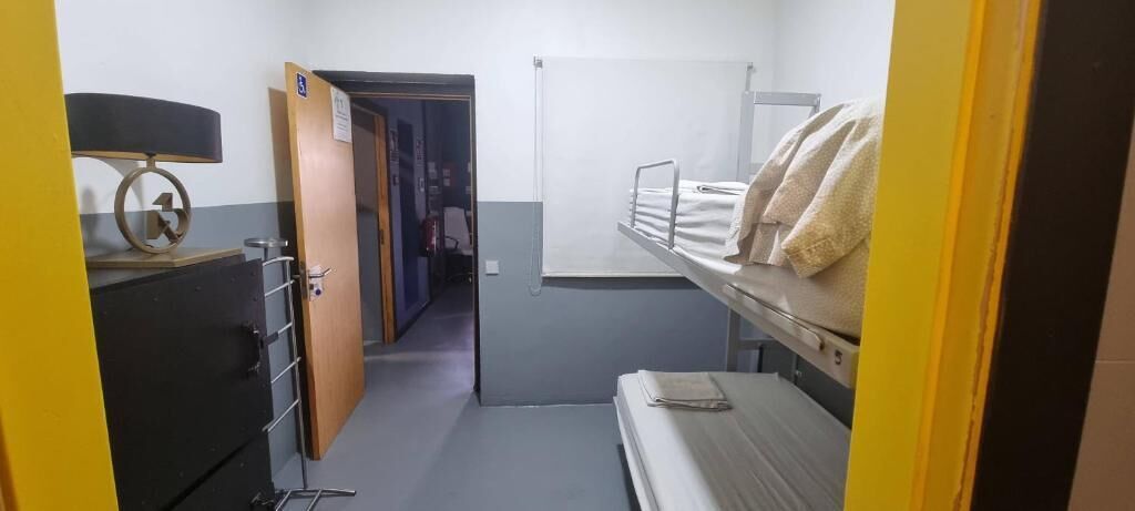 Een kamer met stapelbedden, een bureau met lamp en een deur naar een andere kamer.