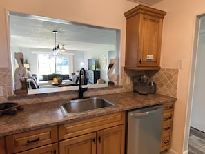 A kitchen with a stainless steel sink, wooden cabinets, a dishwasher, and a large mirror reflecting the living room. - Beautiful 2br 2ba Ocean View Flat! Amazing Views and Location (St Augustine)