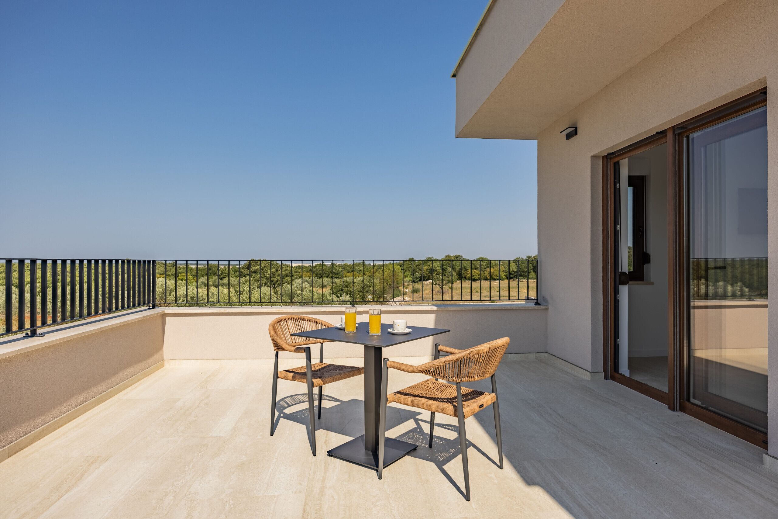 A balcony with a table and chairs, a view of the landscape, and a sliding glass door.