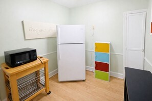 A compact kitchen with a white refrigerator, a black microwave on a wooden cart, and a colorful storage unit.