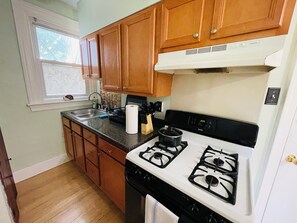 A kitchen with wooden cabinets, a gas stove, a sink, and a window.