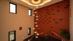 A staircase with a wooden handrail, a brick wall with small windows, and a hanging light fixture with butterflies. - The Heritage Nest Koyla Kund (Darbhanga)