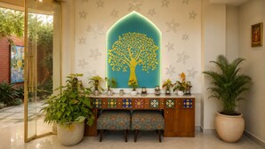 A reception area with a decorative tree mural, a glass door entrance, a wooden console table with patterned tiles, and potted plants. - The Heritage Nest Koyla Kund (Darbhanga)
