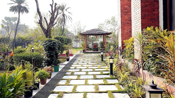 A garden pathway leading to a gazebo, surrounded by potted plants and a brick wall. - The Heritage Nest Koyla Kund (Darbhanga)