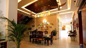 A dining area with a table and chairs, a ceiling fan, and a staircase in the background. - The Heritage Nest Koyla Kund (Darbhanga)