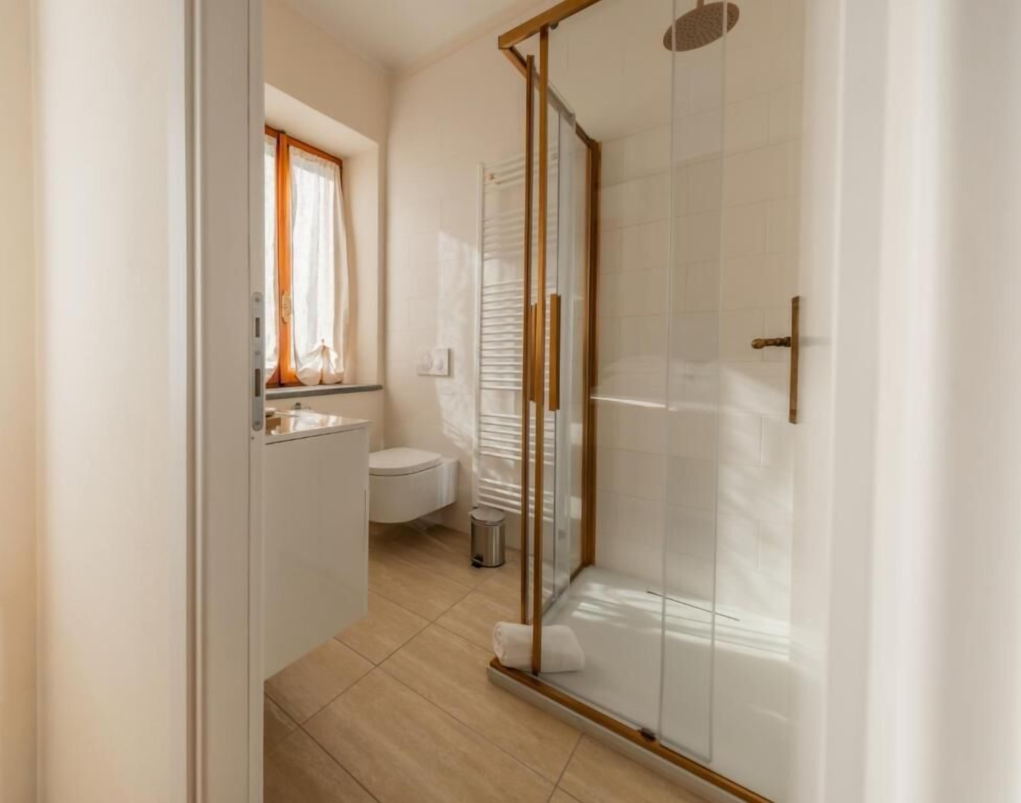 A bathroom with a toilet, a shower with glass doors, and a window with curtains.