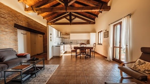 A spacious living area with a fireplace, a dining table with chairs, and a kitchen in the background. - Casa Nizza D'Oro (Castelnuovo Calcea)