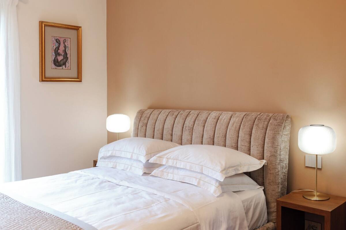 A neatly made bed with white linens, a headboard with vertical ridges, and two bedside lamps on wooden nightstands.