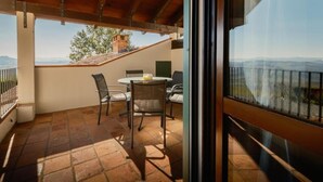 A balcony with a table and chairs, a view of the countryside, and a brick floor. - Casa Nizza D'Oro (Castelnuovo Calcea)
