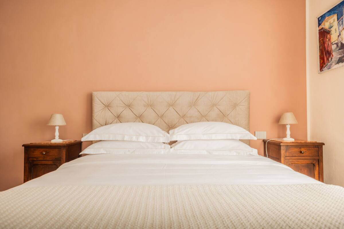 A bed with a tufted headboard, two bedside tables with lamps, and a painting on the wall.