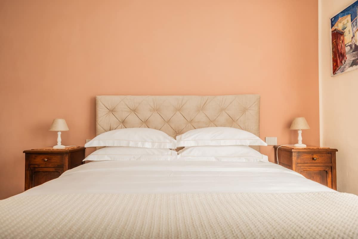Un lit avec une tête de lit capitonnée, deux tables de chevet avec des lampes et un tableau au mur.