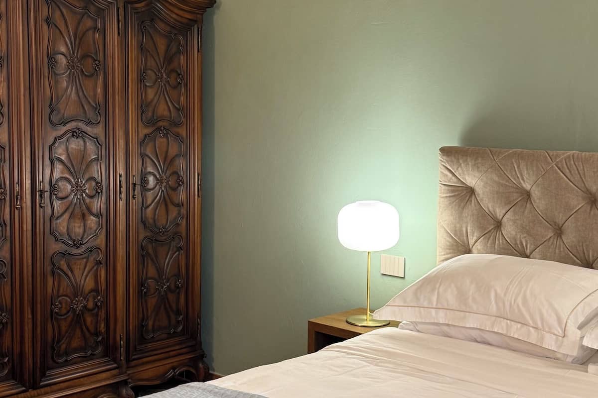 Une chambre à coucher avec une grande armoire en bois, une lampe de chevet, un lit doté d’une tête de lit capitonnée et une table de chevet avec un bloc-notes.