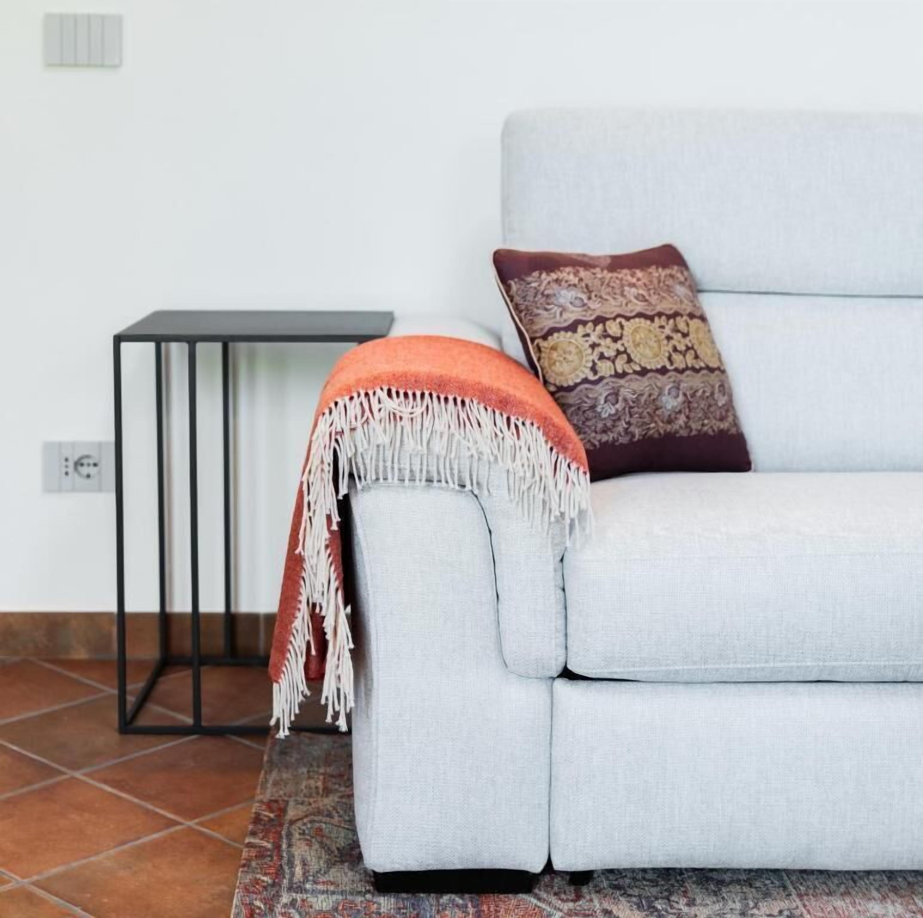 A light grey sofa with a patterned cushion, a small black side table, and a red and white fringed throw blanket.