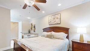 Une chambre à coucher avec un lit en bois, une table de chevet, un ventilateur de plafond et un tableau accroché au mur.