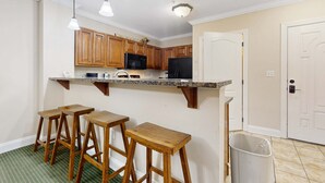 Une cuisine avec des meubles de rangement en bois, un four à micro-ondes, un réfrigérateur et trois tabourets en bois.