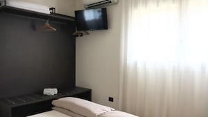 Quarto de hotel com uma cama, televisão fixada na parede, porta-toalhas e ar condicionado.