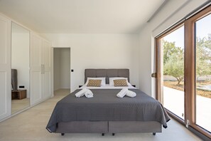 Ein modernes Schlafzimmer mit einem großen Bett, einem Kleiderschrank und einer Schiebetür zum Außenbereich.
