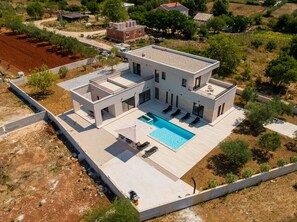 Ein modernes, zweistöckiges Haus mit Swimmingpool, überdachter Terrasse und umzäunter Garten.