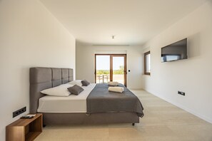 Ein modernes Schlafzimmer mit einem großen Bett, einem an der Wand montierten Fernseher und einer Glastür zum Außenbereich.