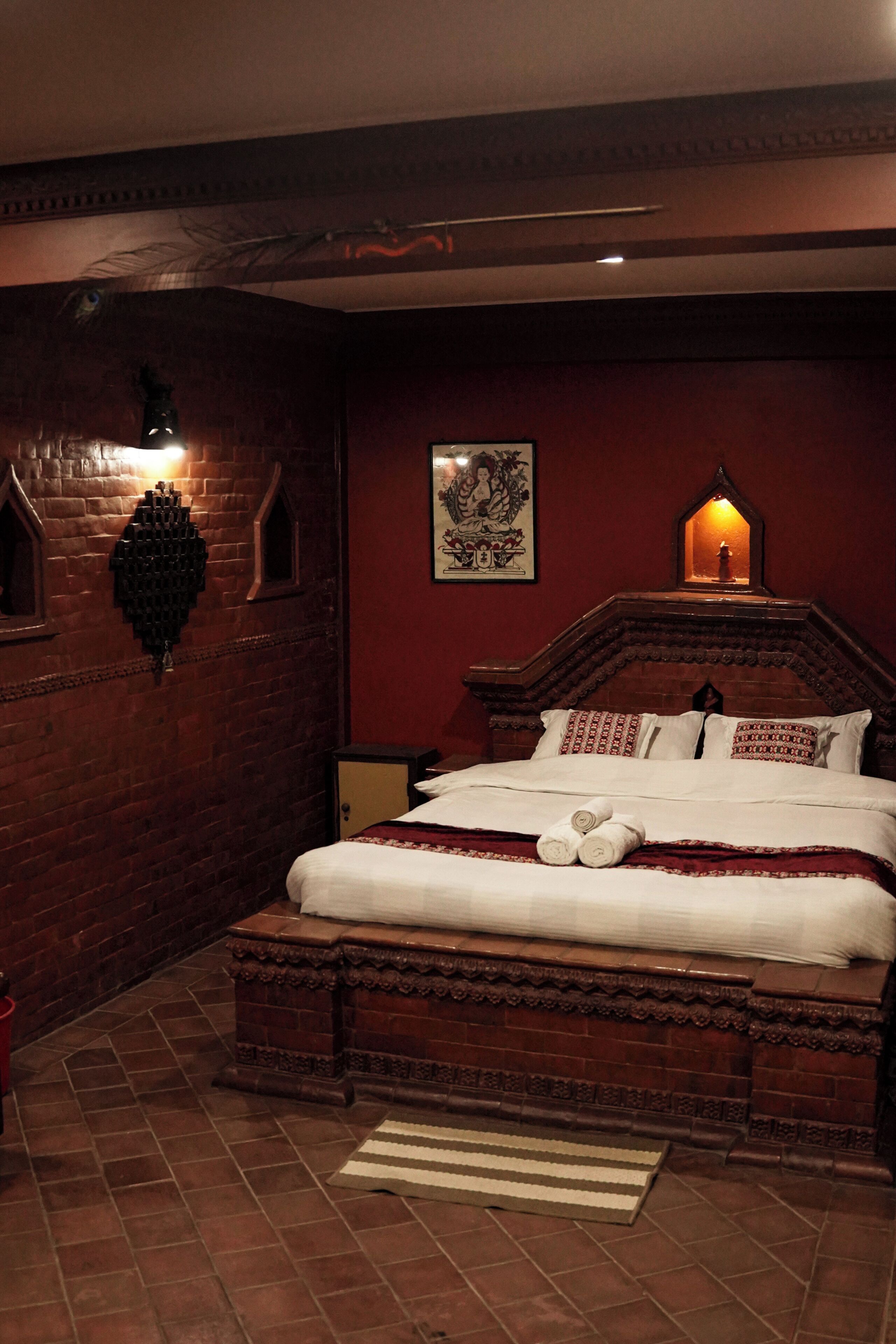 A bedroom with a wooden bed, a red brick wall, a decorative wall light, and a framed picture.