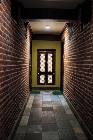 Un pasillo con paredes de ladrillo, piso de baldosas y una puerta con diseño de celosía.