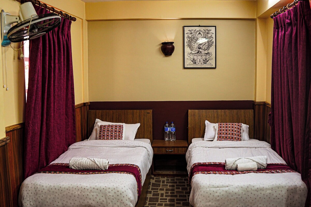 A hotel room with two beds, a wooden headboard, a wall-mounted artwork, and a nightstand with water bottles.