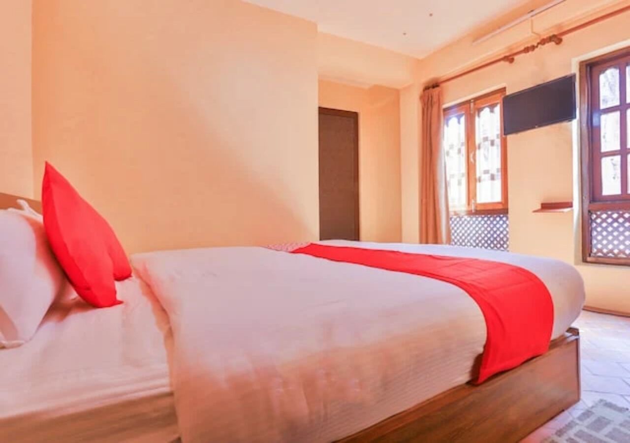 A hotel room with a bed, a wooden headboard, a window with curtains, and a door.