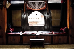 A traditional room with a wooden bench, a small table, and a window with a view of a building. - Hotel Terracotta (Bhaktapur)